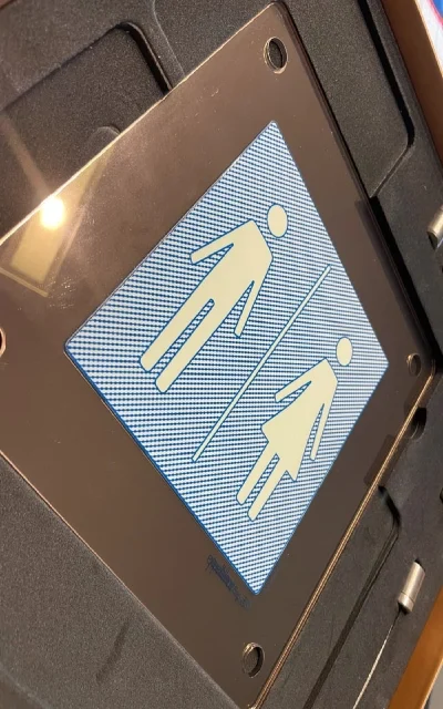 Schild mit Symbolen für Damen- und Herrentoiletten auf einem blauen Hintergrund.