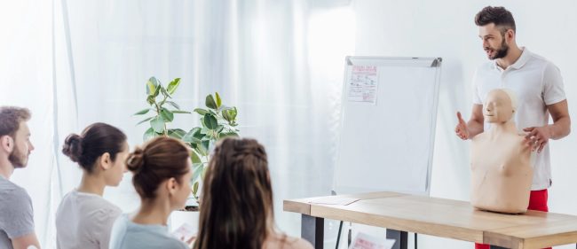 Erste Hilfe Schulung mit Übungspuppe Mann erklärt Erste Hilfe an einer Übungspuppe während einer Schulung mit Teilnehmern.