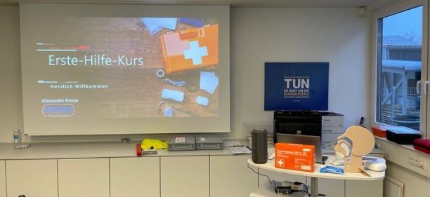 Präsentation für einen Erste-Hilfe-Kurs mit einem Erste-Hilfe-Koffer und einem Dummy auf einem Tisch.